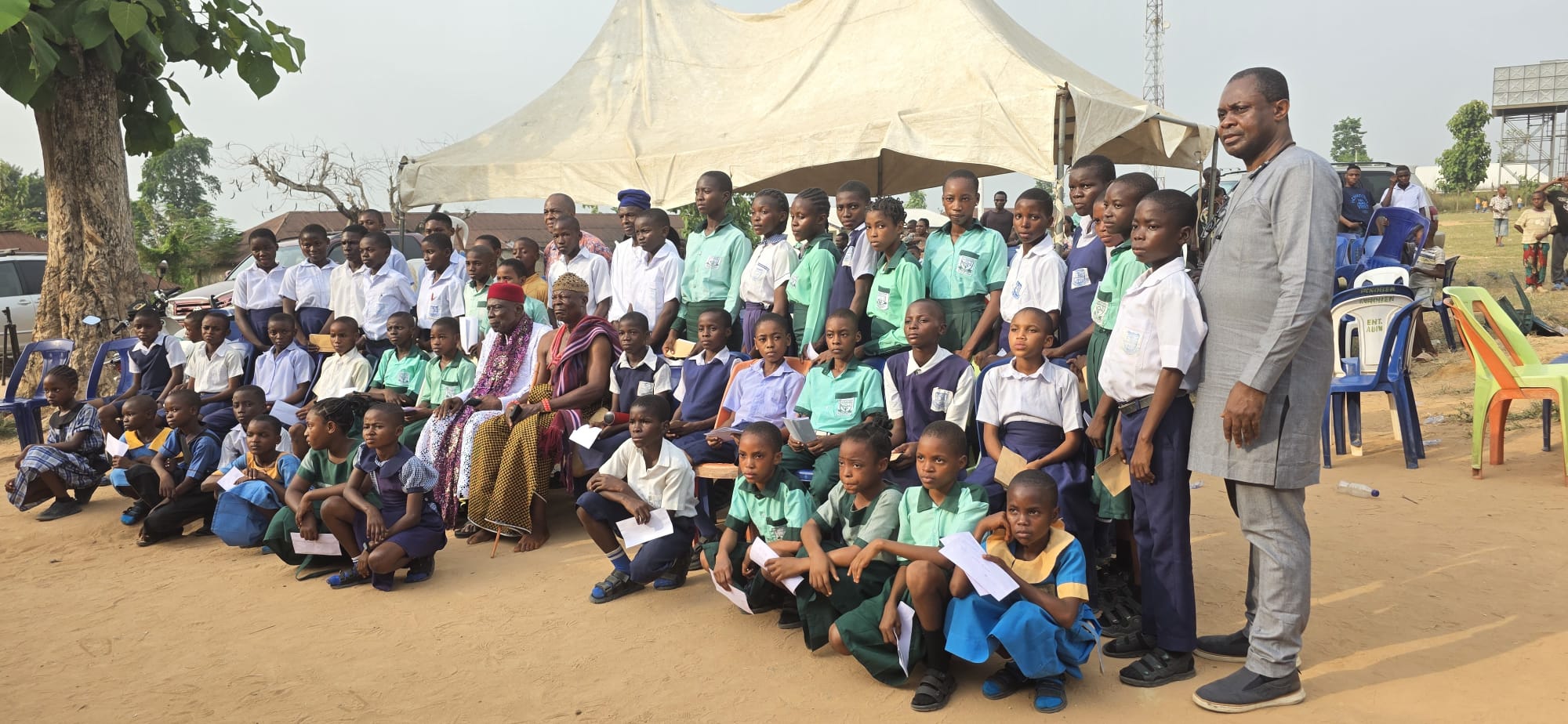 Students and community elders gathered under a tent at a scholarship ceremony in Adim