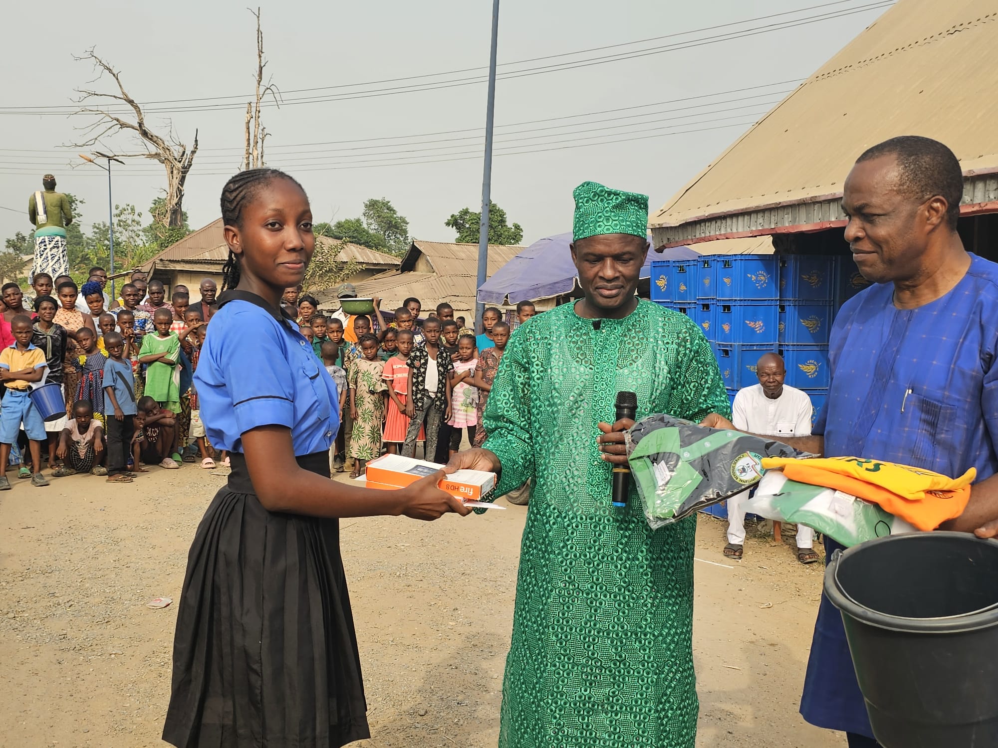 A student receiving a tablet and school supplies, with the community gathered behind her